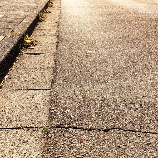 Aufgeheizte Asphaltstraße neben einem Gehweg aus Betonplatten